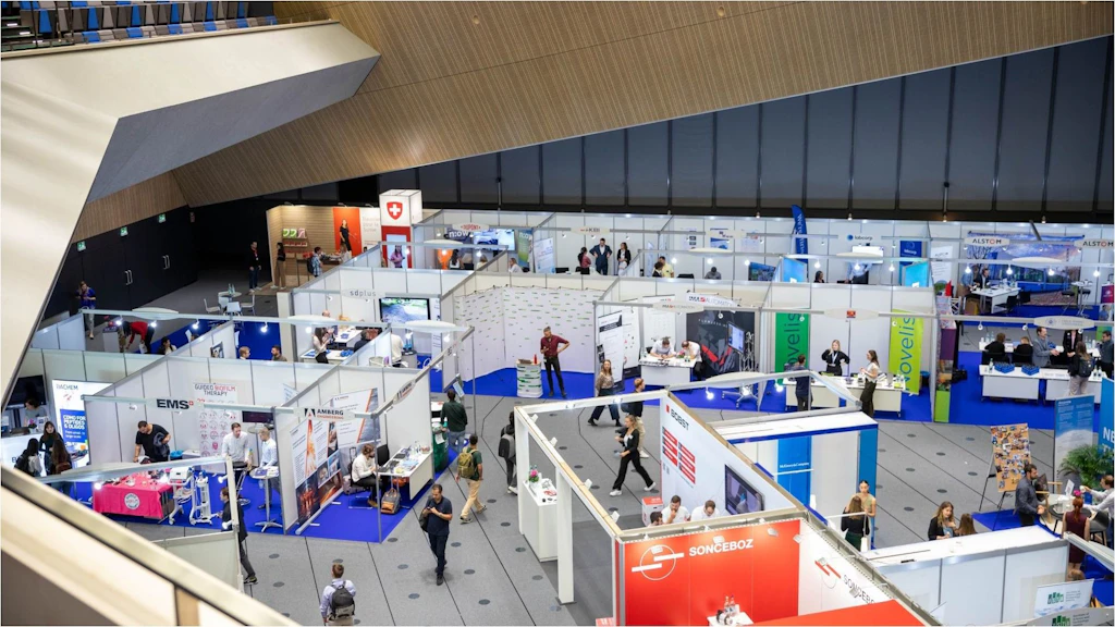 Area espositiva con più stand e persone in un grande padiglione vista dall'alto