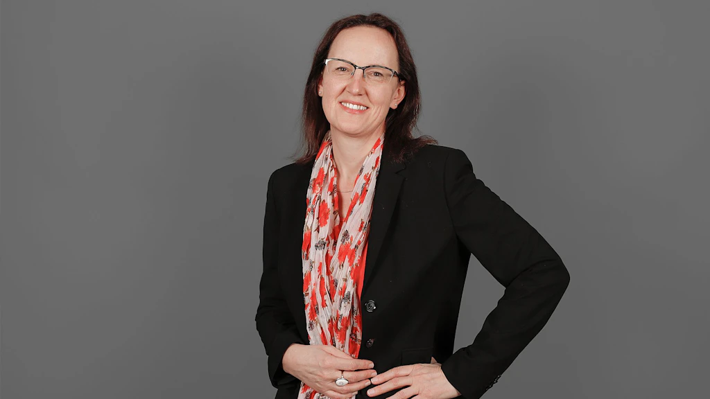 Frau mit schwarzem Blazer und gemustertem Schal vor grauem Hintergrund