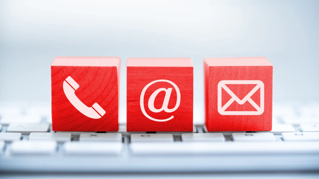 Drei rote Würfel mit weißen Symbolen für Telefon, E-Mail und Brief auf einer Tastatur