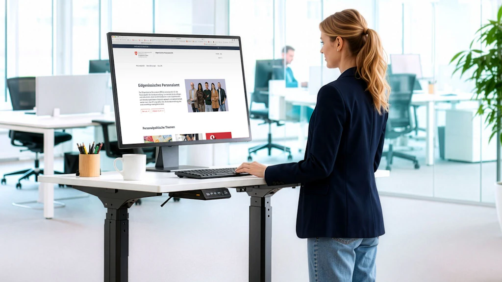 Frau steht an einem höhenverstellbaren Schreibtisch und arbeitet an einem großen Monitor in einem modernen Büro