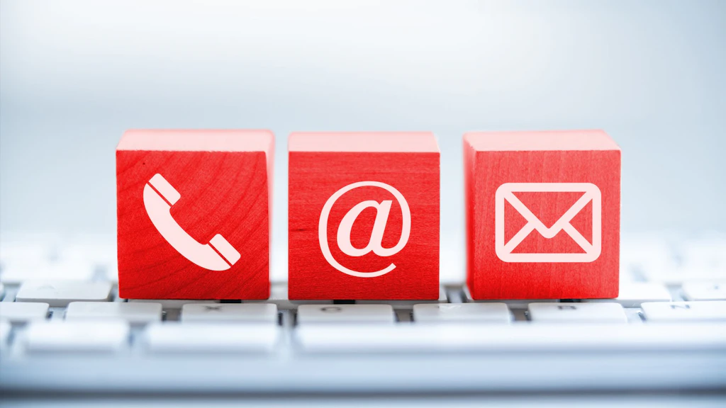 Drei rote Würfel mit weißen Symbolen für Telefon, E-Mail und Brief auf einer Tastatur