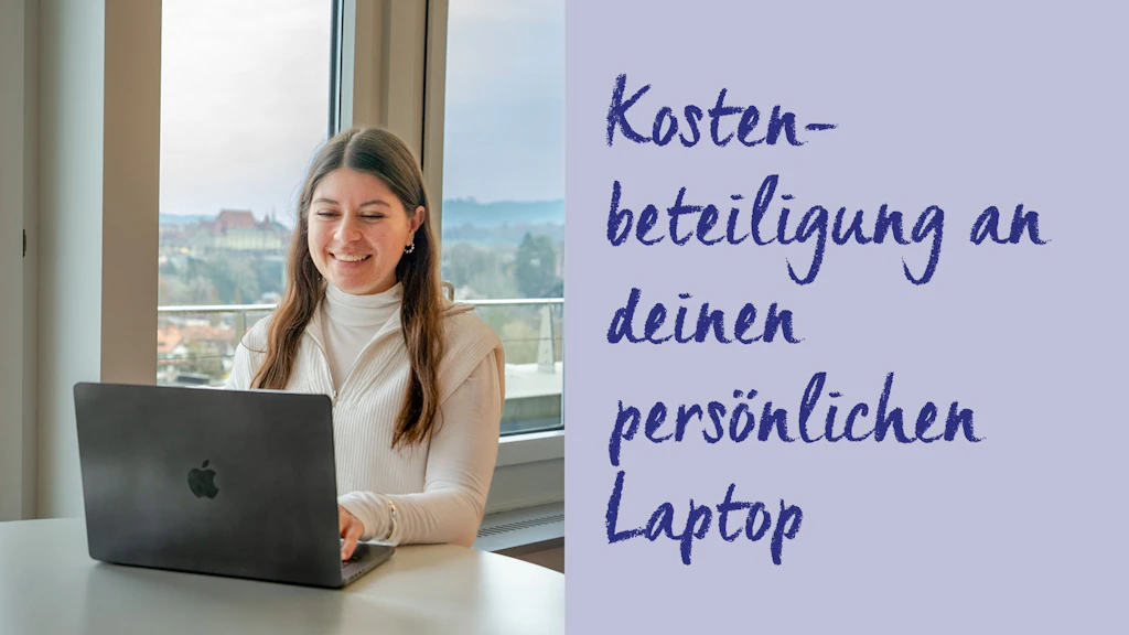 Person sitzt an einem Tisch vor einem Laptop mit Apfel-Logo vor einem Fenster mit Stadtblick