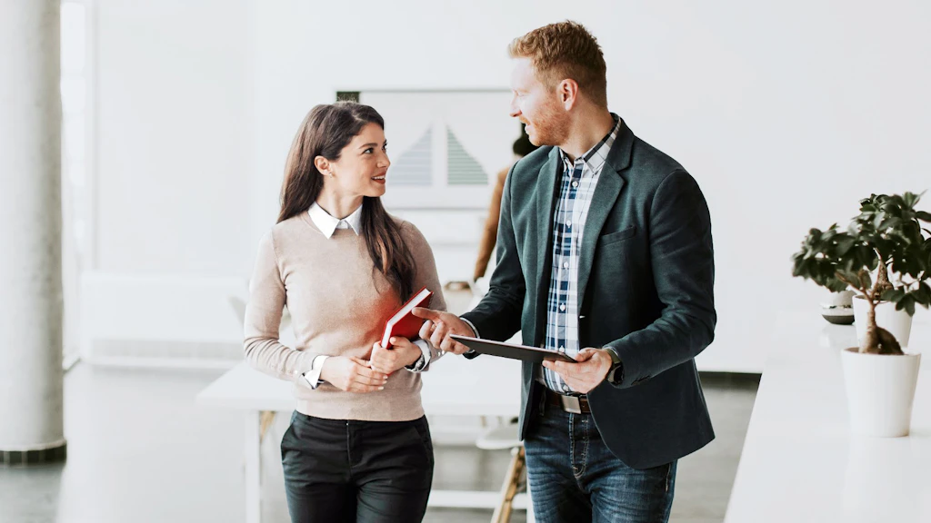 Deux personnes debout en conversation dans un bureau lumineux avec plantes et mobilier moderne