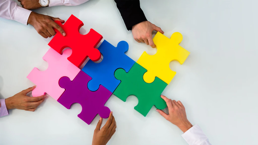 Plusieurs mains assemblent des pièces de puzzle colorées sur un fond clair