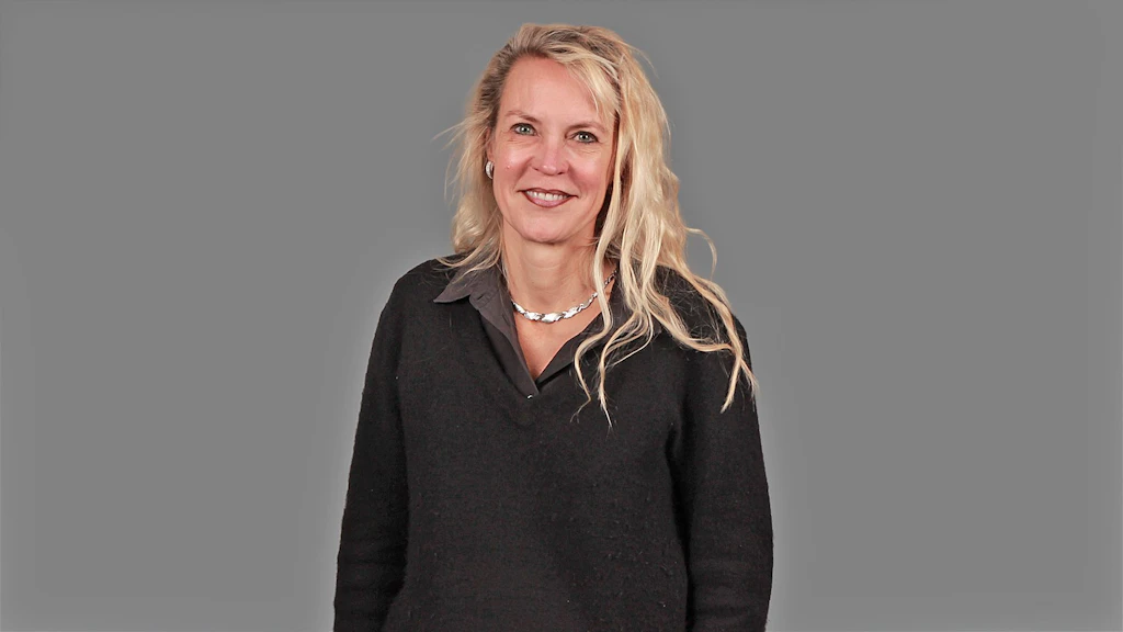 Personne aux longs cheveux blonds, pull noir et collier argenté sur fond gris