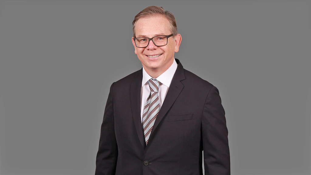 Homme en costume sombre avec chemise blanche et cravate rayée sur fond gris