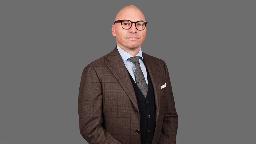 Homme en veste marron à carreaux, chemise bleu clair, cravate à motifs et gilet noir sur fond gris