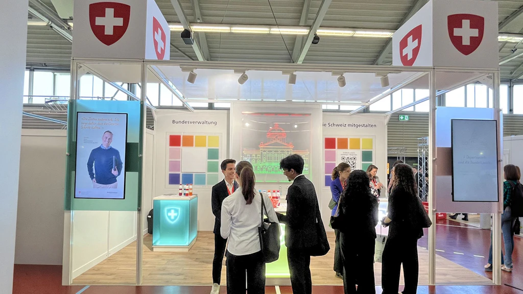 Area espositiva con più stand e persone in un grande padiglione vista dall'alto